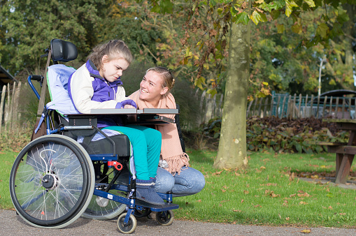 A disabled child in a wheelchair relaxing outside together with a care worker