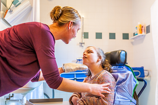 A disabled child in a wheelchair being cared for by a nurse in the bathroom.