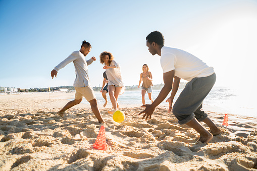 Group of young people playing soccer at the beach and having fun in a summer day