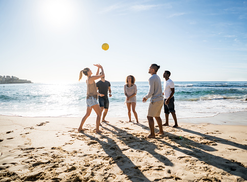 Happy group of young people playing volleyball at the beach and enjoying the summer outdoors