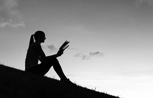Silhouette of woman reading book in the park. Black and white image.