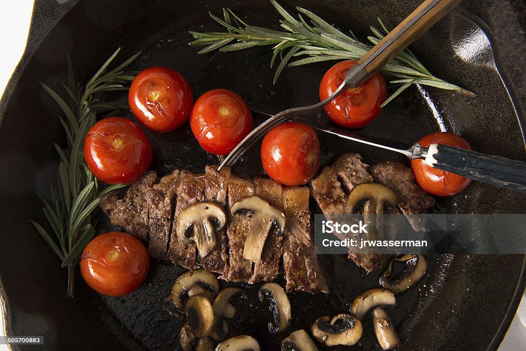 Grilling Strip Loin Steak Series: The Steak is Sliced Series: Grilling Strip Loin Steak in Cast Iron Frying Pan: Steak  is cooked  and sliced  - shown with grilled tomatoes and mushrooms Barbecue Grill Stock Photo