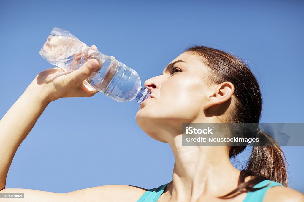 Sportiva donna acqua potabile contro il cielo blu - Foto stock royalty-free di 20-24 anni