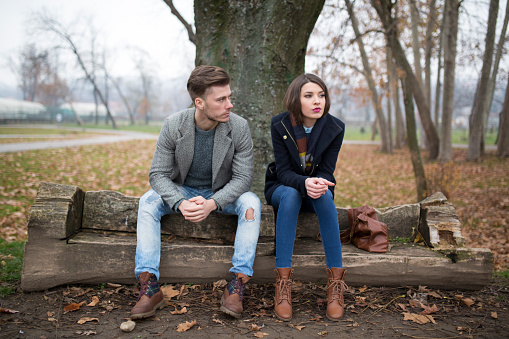 Young couple sitting on the bench in the park, having relationship difficulties.