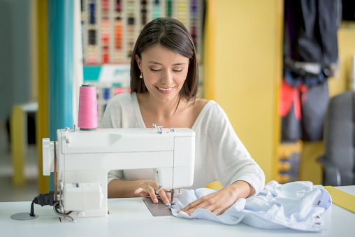 Happy tailor sewing clothes using a machine â fashion concepts