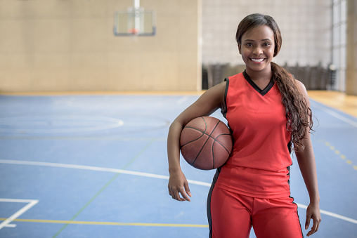 Female African American basketball player holding a ball at the court and looking at the camera smiling