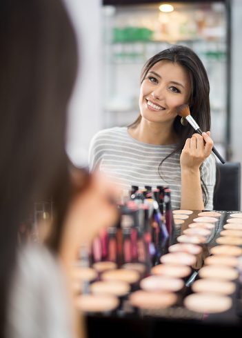 Beautiful Latin American woman putting makeup on and looking very happy