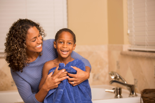 African descent mother uses a towel to dry off her son after his bath.  Home bathroom setting.  