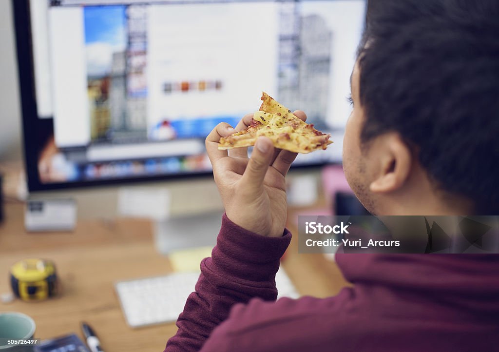 Pizza browsing Cropped shot of a man eating pizza while working at a computer Eating Stock Photo