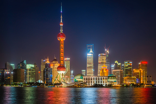 Sweeping panoramic vista across the Huangpu River to the iconic landmarks and futuristic skyline of Pudong, the blue dusk skies glowing above the colourful neon signs of the financial district banks and stock exchange, the soaring spire of the Oriental Pearl Tower, Shanghai World Financial Center and Jin Mao Tower from The Bund in the heart of Shanghai, China's largest city. ProPhoto RGB profile for maximum color fidelity and gamut.