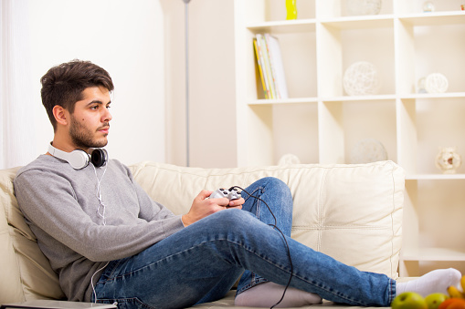 Portrait of excited young man sitting on sofa playing video game - Indoors