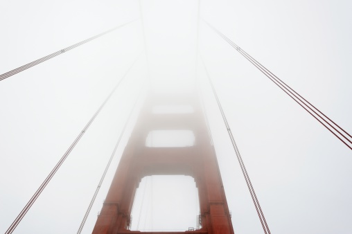 Looking up at support tower to Golden Gate Bridge disappearing into fog.