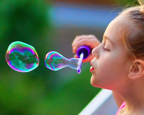 Seven year old girl blowing bubbles outdoors at dusk