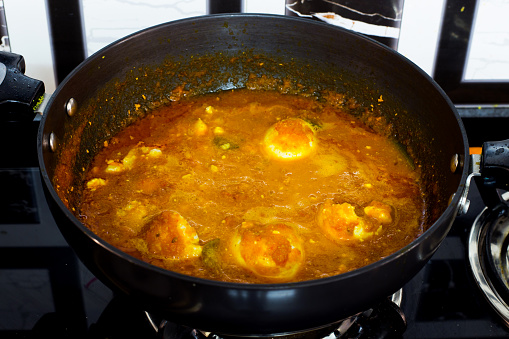 cooking egg curry - a spicy indian dish with fried boiled eggs being cooked in a curry