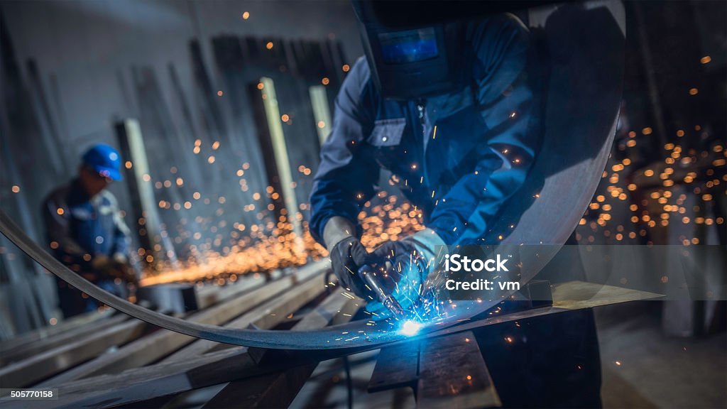 Industrial workers with welding tool Welders with protective equipment welding metal in small workshop. Welder Stock Photo