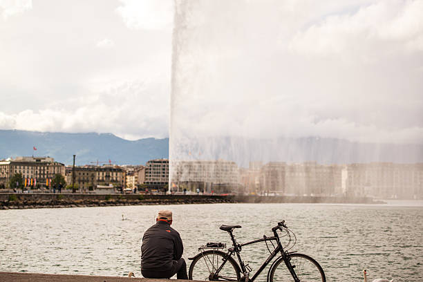 Geneva, Switzerland  - May 11, 2014: Man with bicycle sitting and  looking at Geneva Famous fountain - Jed d'Eau, Switzerland