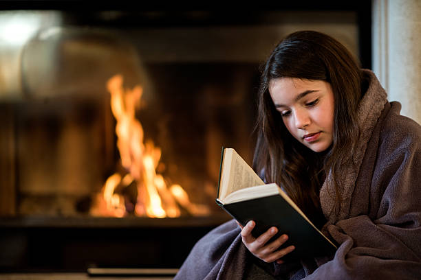 istock Girl reading a book by the fireplace 505780568
