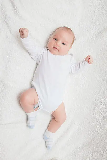 Newborn baby in white romper on white textile background