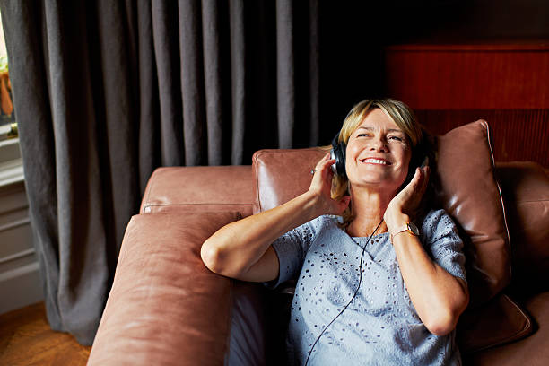 Let music into your soul Shot of a mature woman lying back on her sofa listening to music on headphones older woman eyes closed stock pictures, royalty-free photos & images