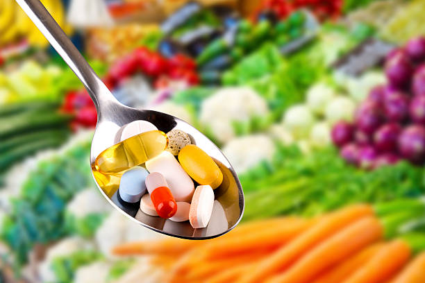 spoon with pills, dietary supplements on vegetables background spoon with variety of pills, dietary supplements on blurred vegetables background food supplements stock pictures, royalty-free photos & images