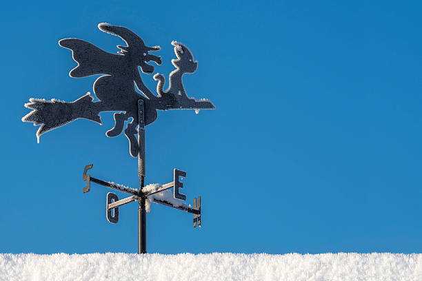 The weather vane witch with her cat - sitting in front of her - is riding her broomstick northbound in sunny winter weather with clear blue skies. The roof on which the weather vane is mounted is covered with fresh snow. The weather vane is frosted with ice crystals (frozen water from humidity in the air). Whereas many birds fly south in (or before the winter), this witch is heading north for even colder climate.
