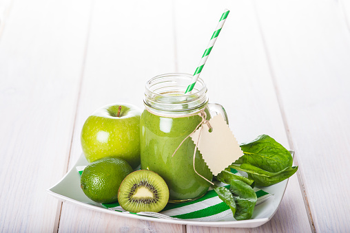 Green smoothie and fresh ingredients on a white wooden background