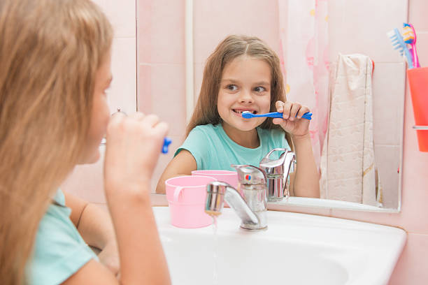 6 歳の少女ブラッシングフロントの歯スタイルのミラーのバスルーム - smiling human teeth toothbrush moving up ストックフォトと画像