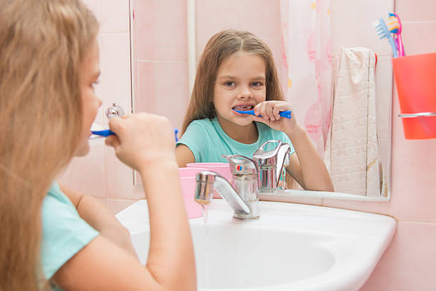 fille de six an nettoie les dents côté regardant le miroir de la salle de bains - smiling human teeth toothbrush moving up photos et images de collection