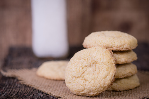 Sugar cookies piled up with jar of milk blurred in background.