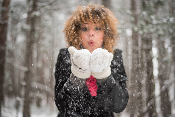 Portrait of young woman blowing snow of her gloves in woods,grain added
