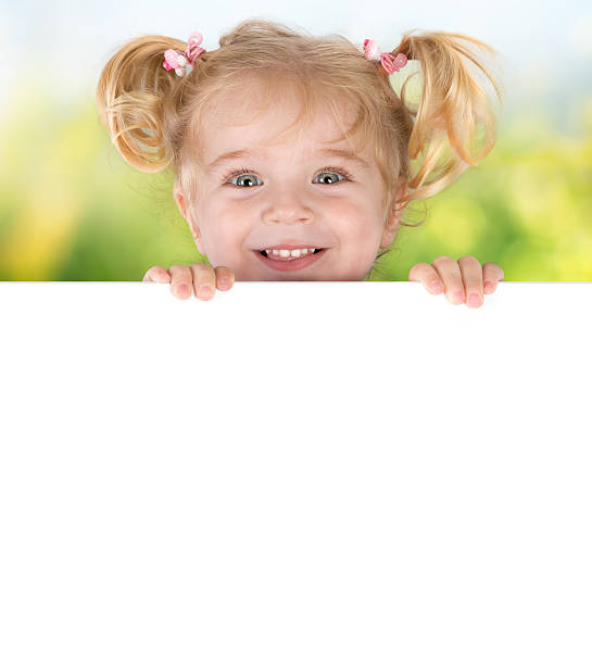 Smiling little girl peeking behind a board blonde girl emerges from a billboard peeking photos stock pictures, royalty-free photos & images