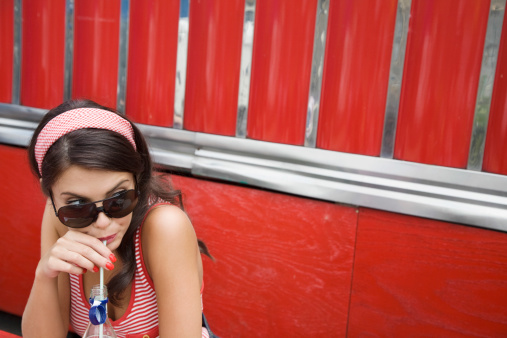 Closeup of a young woman in sunglasses drinking soda
