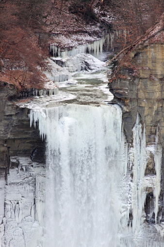 Winter view of icy creek flowing over Taughannock Falls near Ithaca, in the Finger Lakes Region of New York State.  Vertical, waterfall.