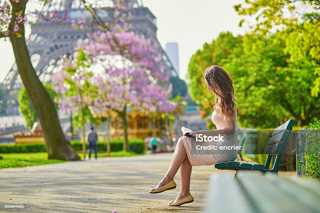 Beautiful young woman in Paris, reading a book Beautiful young woman in Paris, near the Eiffel tower on a nice and sunny spring day, reading on the bench outdoors Paris - France Stock Photo