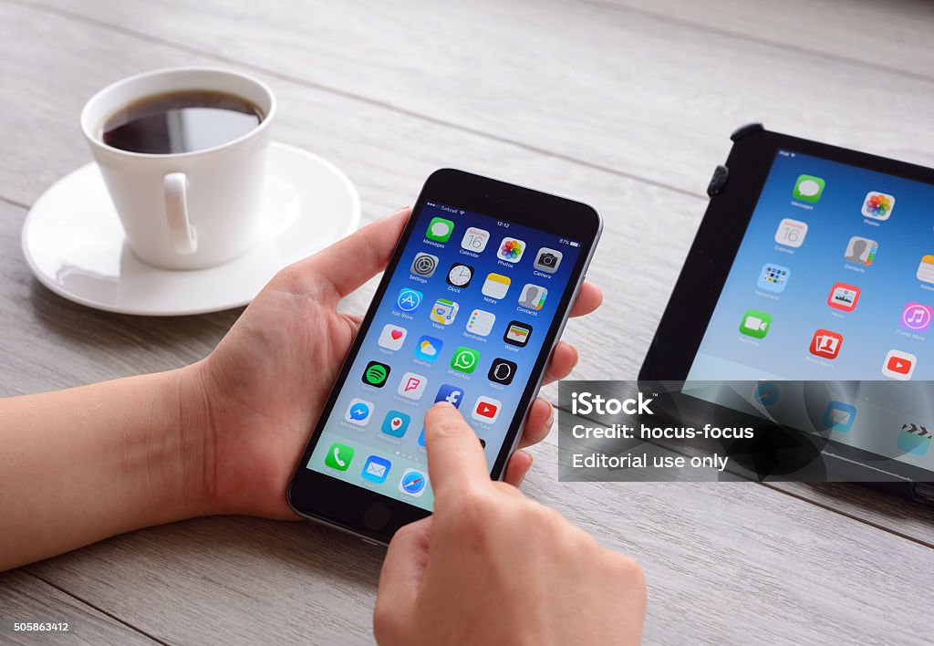 Using Apple iPhone smart phone İstanbul, Turkey - January 16, 2016: Woman hands holding an Apple iPhone 6 Plus displaying home screen. An Apple iPad Mini on the desk. iPhone and   iPad, produced by Apple Computer, Inc. Adult Stock Photo