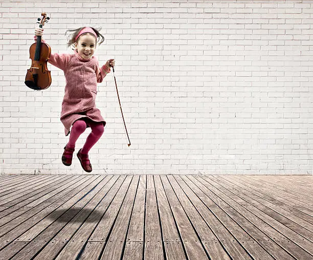 little girl with violin jumping on a room with white bricks wall and wood floor