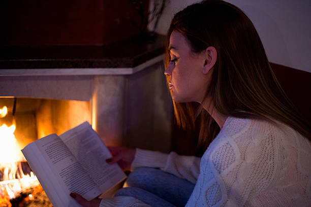 istock woman reading a book by fireplace 505869272