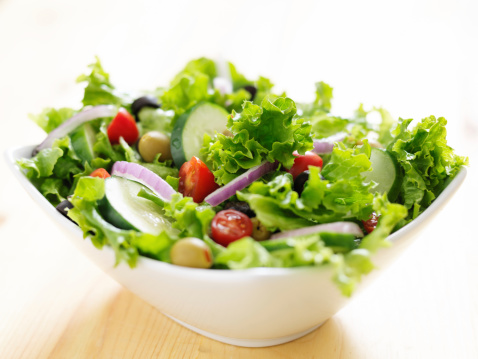 bowl of leafy green salad with olives, tomatoes and cucumber.