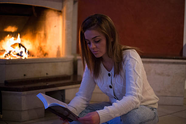 istock woman reading a book by fireplace 505869618
