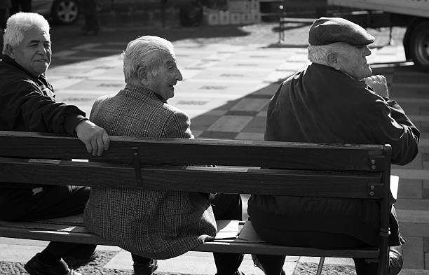 Militello Val di Catania (Sicily), Italy- December 2, 2011: Three senior men--one wearing the Sicilian coppola cap--sit on a bench in the main piazza in Militello Val di Catania, Sicily.