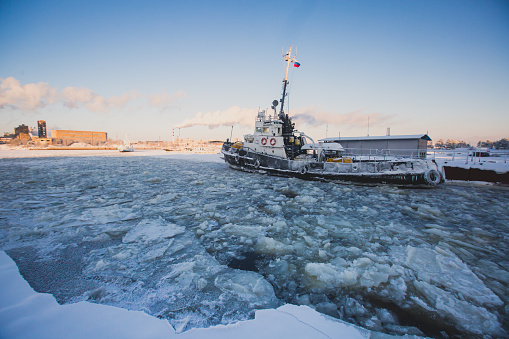 The Icebreaker tug boat ship trapped in ice tries to break and leave the arctic bay, in the sunny winter day