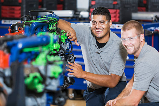 Two multi-racial men in auto mechanic school with engine Two multi-ethnic young men in vocational school, taking a class on reparing diesel engines.  They are working on an engine that has had parts painted different colors for training purposes.  They are wearing safety glasses. The focus is on the Hispanic man. multiengine stock pictures, royalty-free photos & images