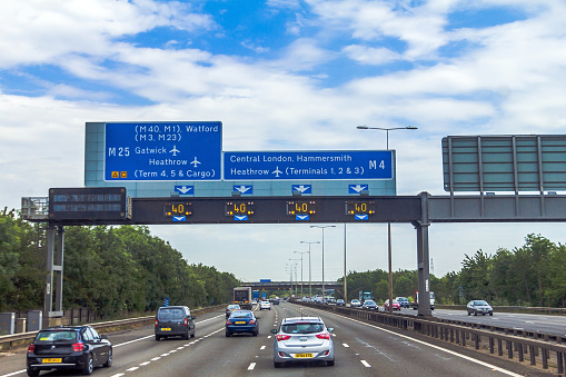 London, UK - June 5, 2015: Intensive left-hand traffic on British four lane motorway M4 between Windsor and London  with active electronic overhead information sign at grey cloudy  summer day
