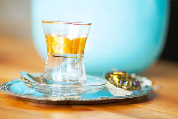 Small tea glass with golden details on tray with tea egg on table, tea with flowers inside