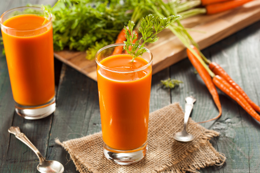 Fresh carrot juice in glass cup on a wooden reamer. Selective focus