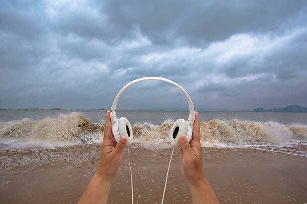 hand holding earphone on beach,listening to waves
