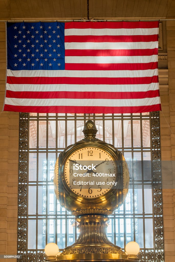Grand Central Terminal New York, USA - January 13, 2016: The famous four sided clock in the center of Grand Central Terminal late in the day with an American flag hanging in the background.  American Flag Stock Photo
