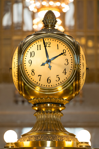 New York, USA - January 13, 2016: The famous four sided clock in the center of Grand Central Terminal late in the day with an illuminated chandelier  hanging in the background.