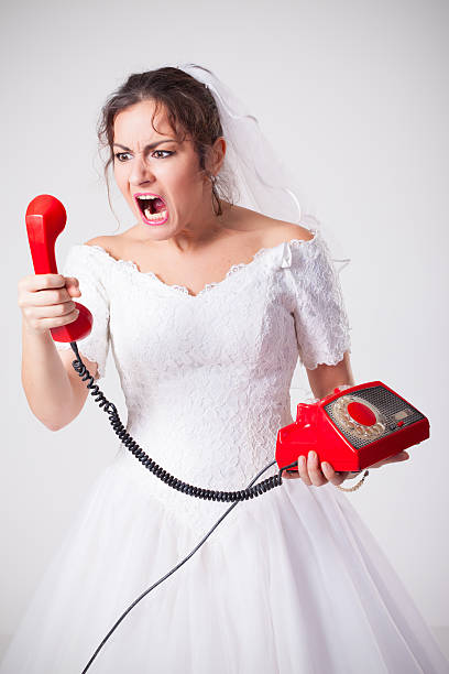 Studio portrait of mad bride holding old retro red phone and screaming out loud. Nerdy bride is looking really mad.