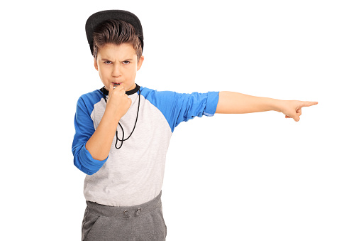Studio shot of an angry kid in sportswear blowing a whistle and pointing right isolated on white background